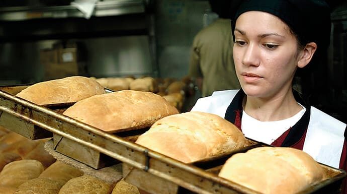 La dignidad del trabajo en la era técnico-industrial Trabajadora en un horno de pan mostrando esfuerzo y dedicación en su labor diaria.