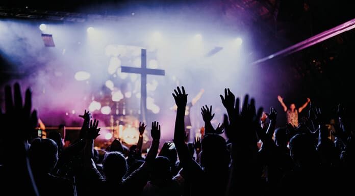 Dios, a la moda Jóvenes con los brazos en alto durante un concierto, símbolo de búsqueda colectiva y emoción compartida